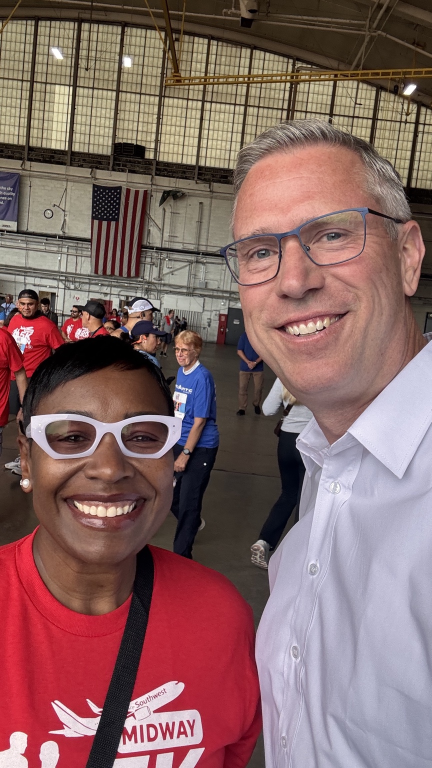 Two people smiling together at a Midway event in an aircraft hangar