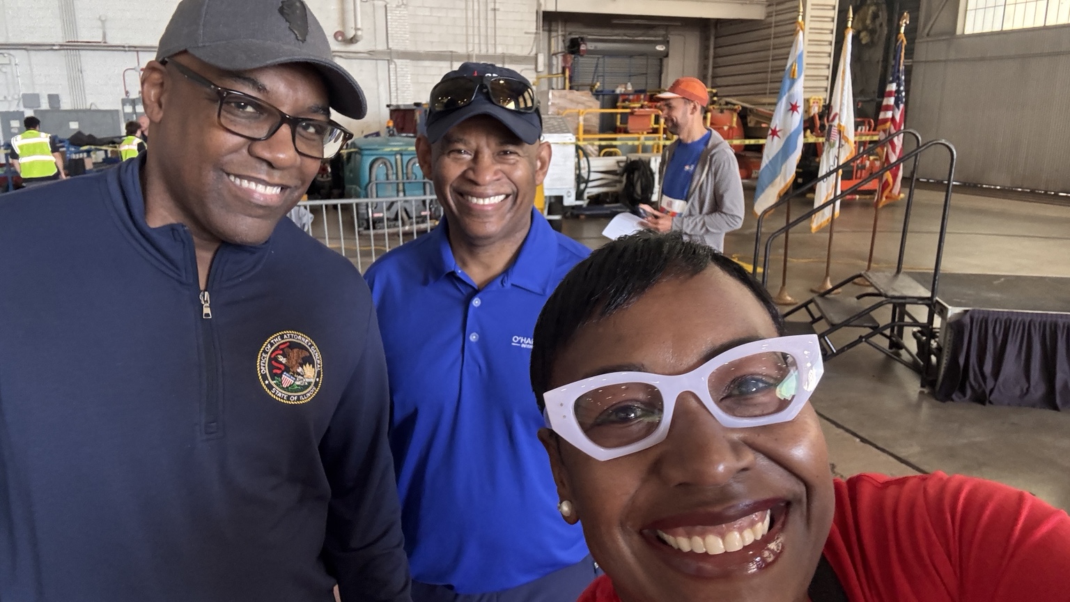 Three people smiling together at an event in an aircraft hangar