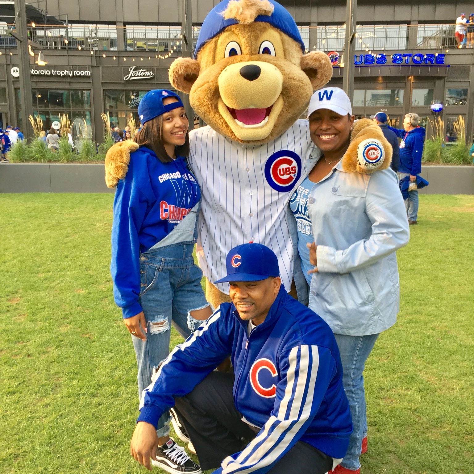Three people in Chicago Cubs apparel posing with the Cubs mascot