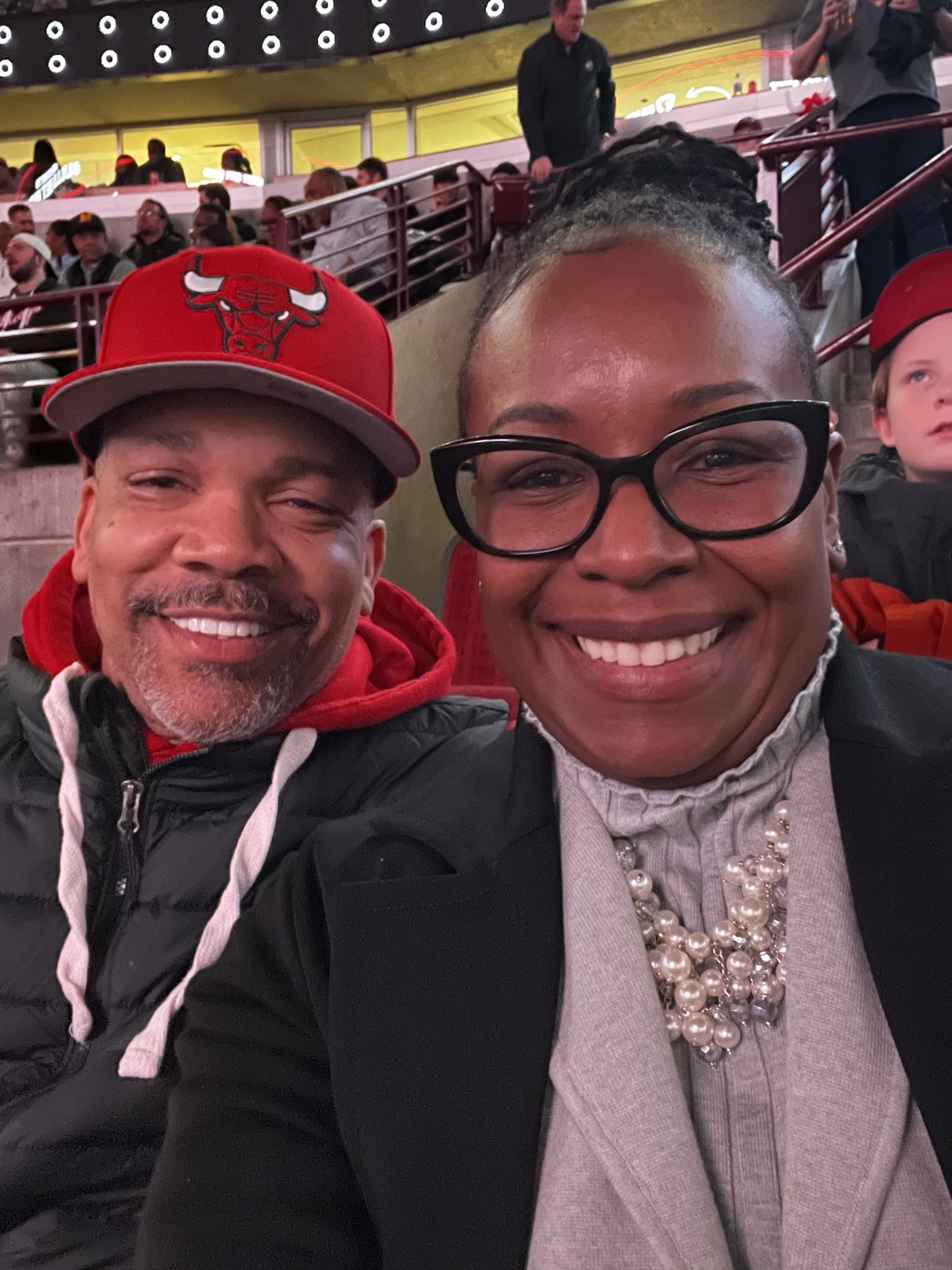 Two people smiling together in stadium seats, with a Chicago Bulls cap