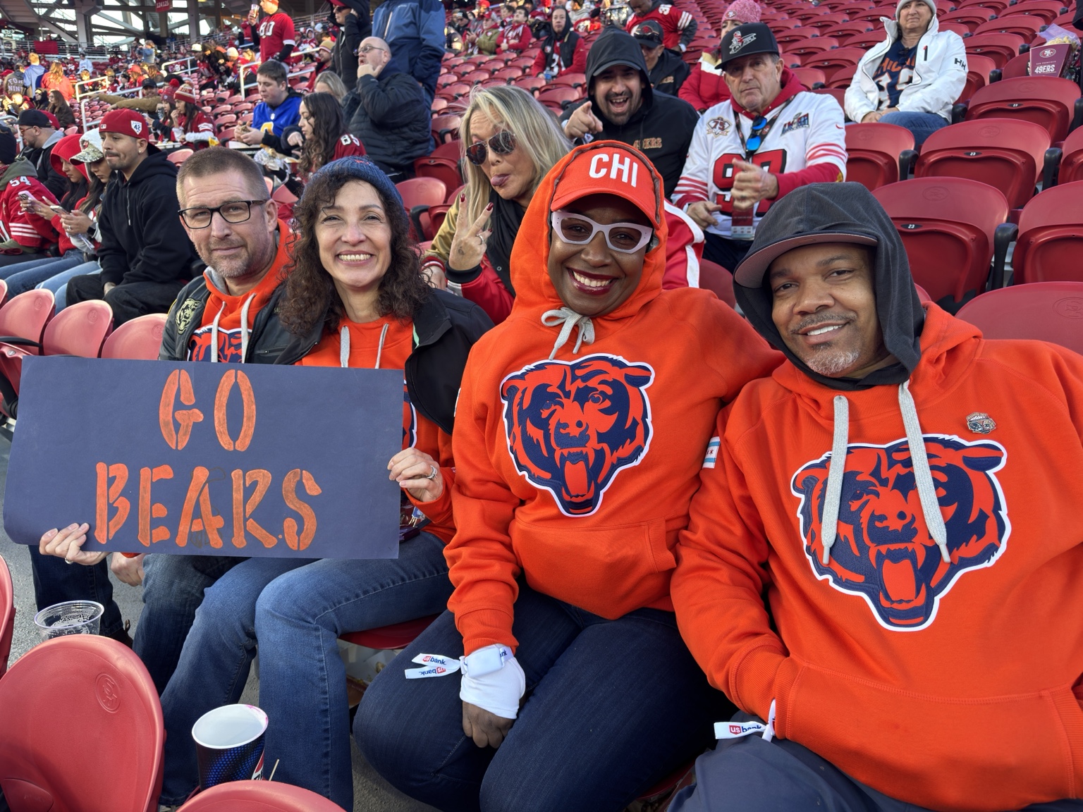 Chicago Bears fans in orange hoodies holding a Go Bears sign at a football game