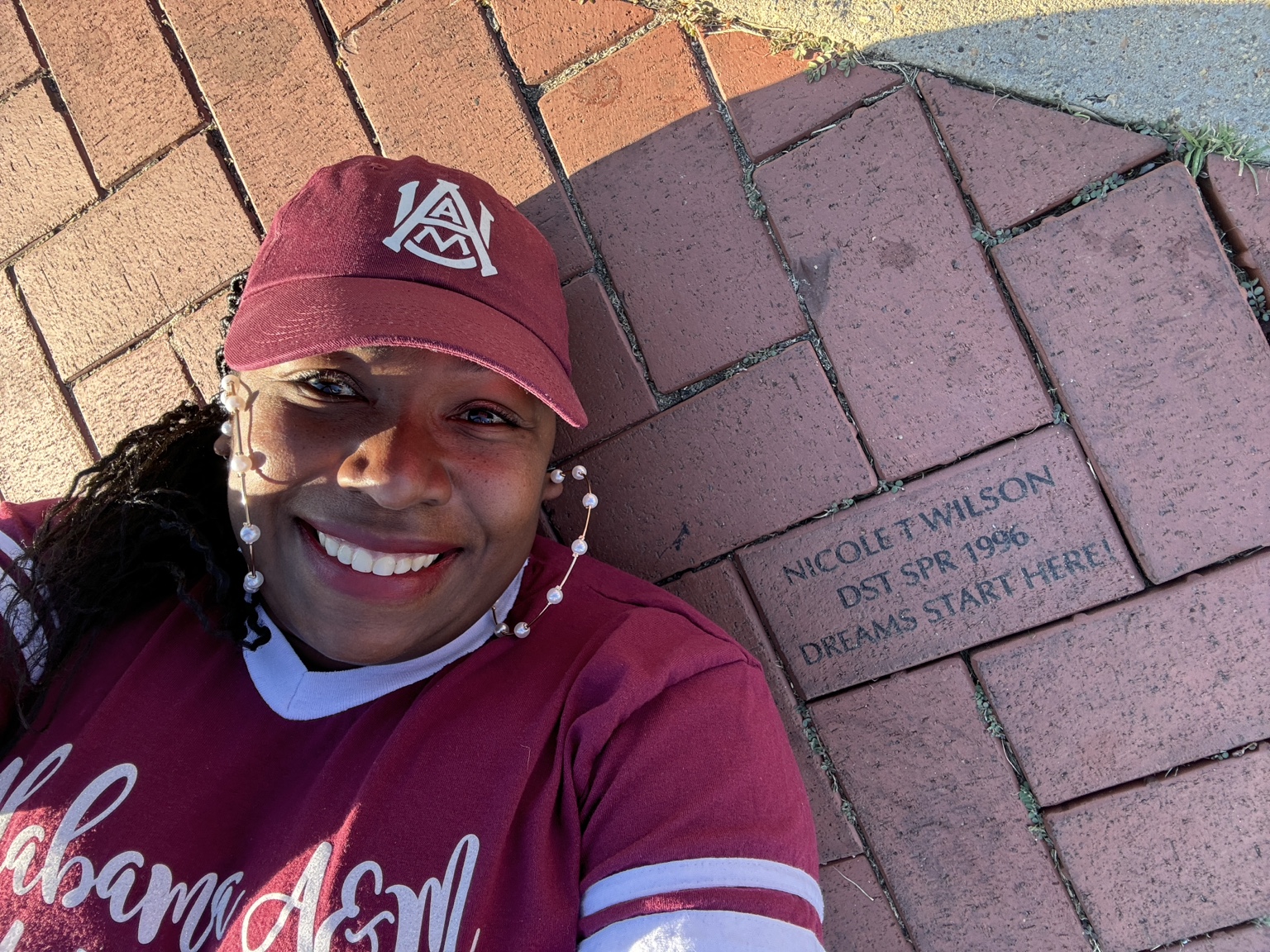 Smiling in Alabama A&M apparel beside a commemorative brick reading DST Spring 1996 and Dreams Start Here