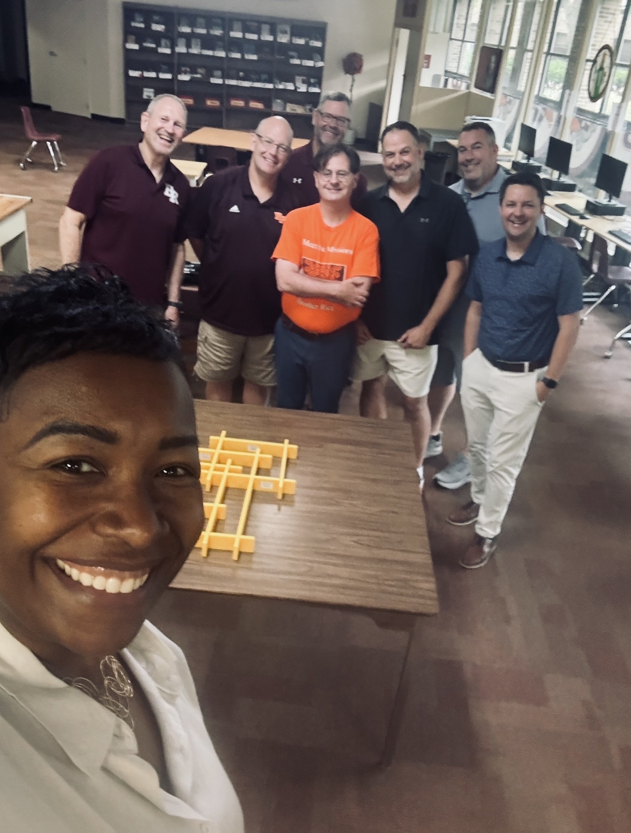 A smiling group gathered around a table with a yellow construction activity in a classroom